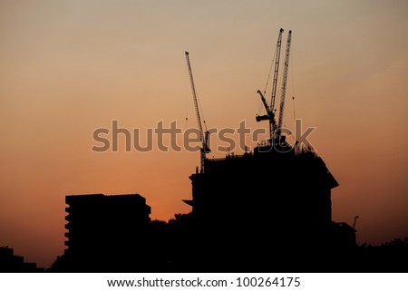 House under construction and tower cranes on the background of the setting sun