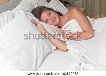 A young attractive woman lying on a bed with white sheets
