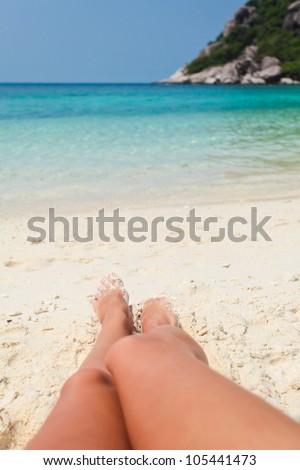 Legs of young woman lying in the sand on the beach against of ocean and sky
