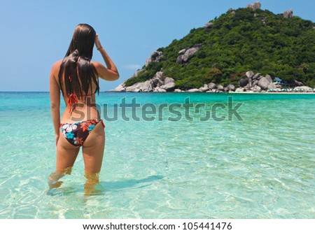 Beautiful young woman in swimsuit is in the water at the seashore. View from the back