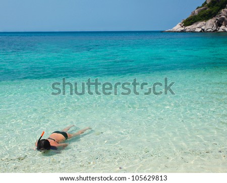 Woman in diving mask swimming in clear water along the beach