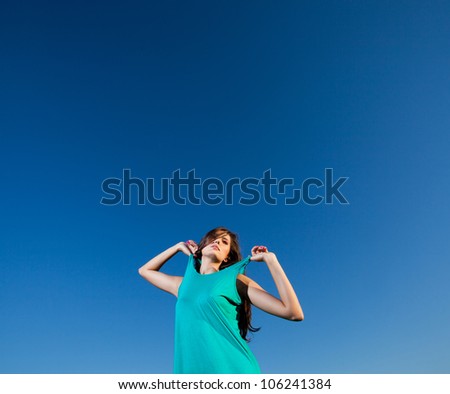 Pretty woman pulls straps of her blue dress against the blue sky