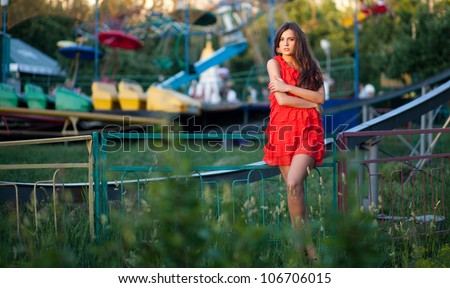 Pretty woman in a bright red dress leaning on the railing of the rides which out of work