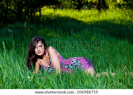 Young woman in a light violet dress lying on the grass leaning on it with one hand