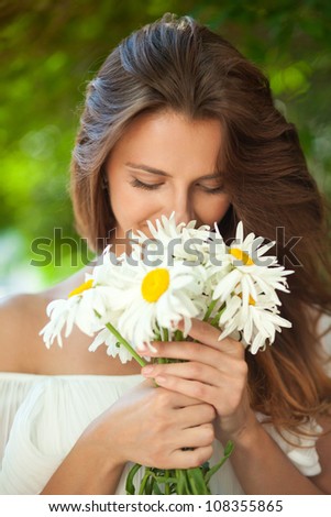 Young woman smelling a bouquet of daisies, which in her hands. Close-up