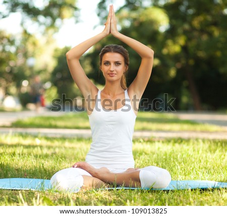 Beautiful woman practices yoga in nature. Lotus pose, hands over her head