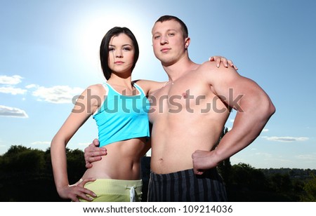 Beautiful young athletic man and woman standing next to each other against the blue sky