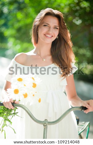 Beautiful young woman in a white summer dress and daisies in her hand clinging to an old bicycle handlebars
