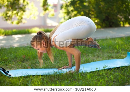 Beautiful woman practices yoga in nature; standing on the hands, knees lying on the shoulders