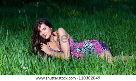 Beautiful woman in a light violet dress lying on the grass leaning on it with one hand