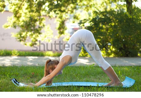 Beautiful young woman practices yoga on the nature, standing on her feet and hands, buttocks up
