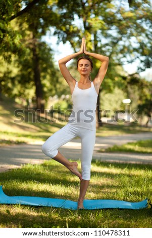 Beautiful woman practices yoga in nature. Standing on one leg, hands over her head