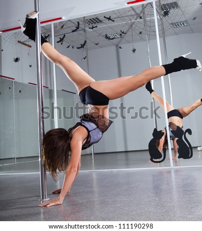 Young woman in a suit for the pole-dance standing on her hands. One leg hold on a pole