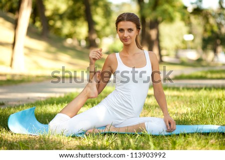 Beautiful young woman practices yoga in nature; holding the foot of the same name by hand