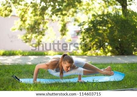 Beautiful young woman practices yoga in nature; standing on the hands, knee lying on the shoulder