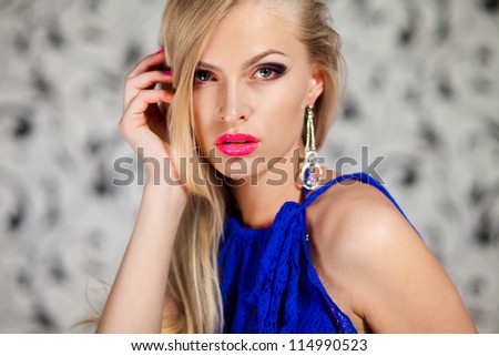 Portrait of glamour young woman in blue dress against the gray vintage wallpaper