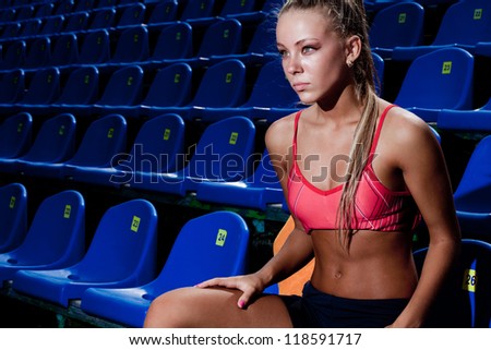 Beautiful young woman in a sports suit sitting on the stadium seat