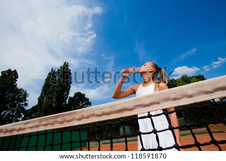 Beautiful young woman in a white tennis dress drinking water from a bottle