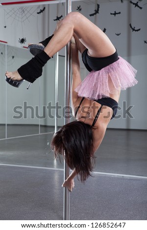 Beautiful woman in a suit for the pole-dance performing acrobatic exercise on the pylon