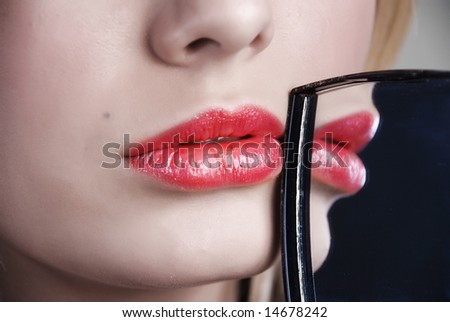 Scarlet lips are reflected in a little mirror which a girl holds in a hand