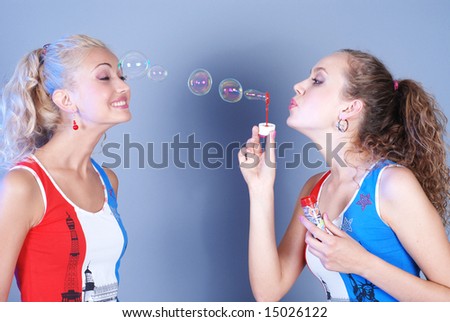 Two beautiful girls dressed in identical shirts play, inflating soap-bubbles