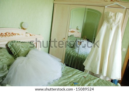 A bedroom in which standing the closet of clothes and bed. A white bridal veil lies on a bed, a wedding-dress hangs on a closet