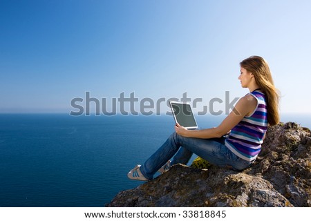 woman sitting on the rock with laptop near the sea