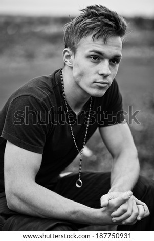 Handsome young man sitting and thinking about something with field in the background. Black and white