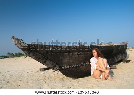 Young woman sitting near the black wooden boat
