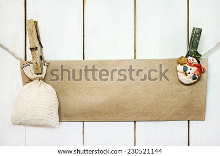 Christmas snowman clothespines hanging on clothesline or rope and holding brown craft paper card and sack on wood background