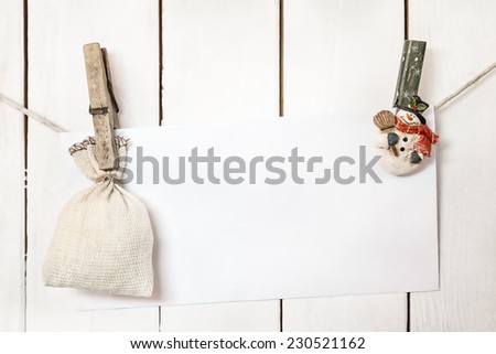 Christmas snowman clothespines hanging on clothesline or rope and holding white blank paper card and sack on wood background