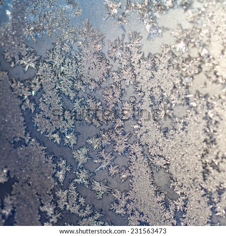Frozen snowflakes and frost magic pattern with sunlight on Christmas winter window. Colored in gray or silver and blue tone. Selective focus with blur edges of image