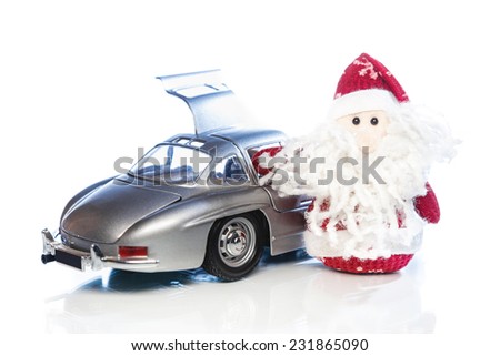 Santa Claus or Father Frost with old vintage automobile on white background with reflection. Main focus of image on Santa Claus and selective on turned the back side and opened left door toy retro car