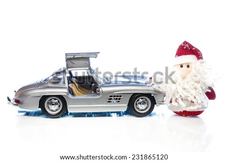 Santa Claus or Father Frost with old vintage automobile on white background with reflection. Main focus of image on Santa Claus and selective on the side turned and opened doors toy retro car