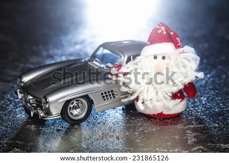 Santa Claus or Father Frost with old vintage automobile on on silver or metal grunge surface with backlight from behind. Main focus of image on Santa Claus and selective on turned left toy retro car