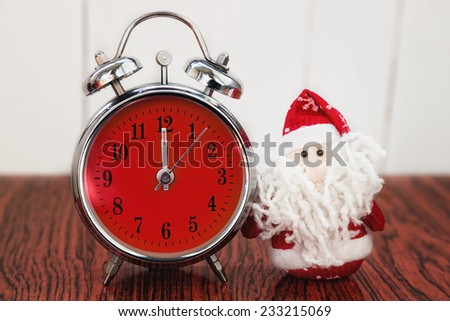 Santa Claus or Father Frost and vintage alarm clock with red dial on wooden background. Showing time twelve midnight