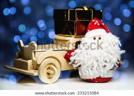Santa Claus and old vintage wooden automobile with gift box on christmas lights background. Main focus of image on Santa Claus and selective on turned left wood car with gift box