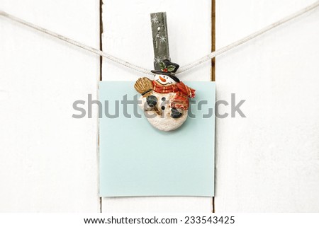 Christmas snowman clothespins hanging on clothesline or rope and holding light blue blank note paper card on wooden background
