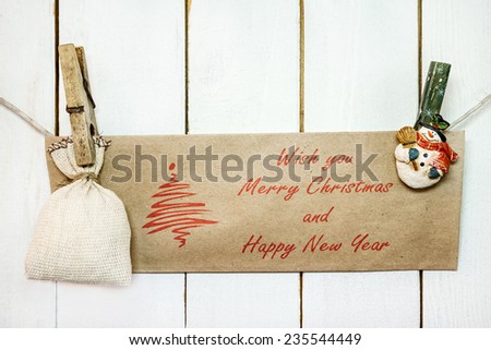 Christmas snowman clothespins hanging on clothesline or rope and holding brown Christmas greeting card and sack on wood background