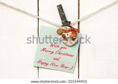 Christmas snowman clothespins hanging on clothesline or rope and holding light green greeting note paper card on wooden background