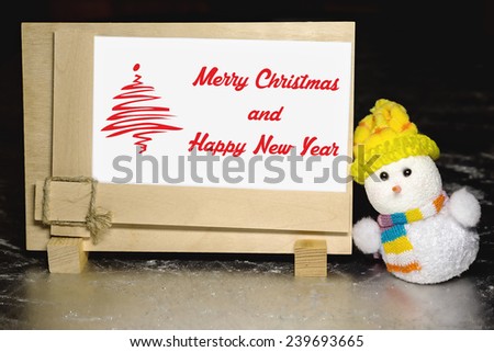 Christmas greeting card with snowman toy and greeting blank wooden frame on silver or metal grunge surface