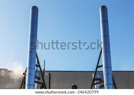 Smoke metal pipes on rooftop of industrial building against blue sky background