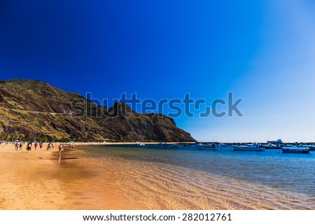 Beach Las Teresitas with water and waves on yellow sand on coast or shore of Atlantic ocean on Tenerife Canary island, Spain. Blue sky and mountain at the background