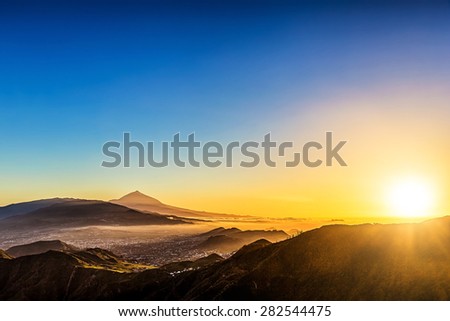 Sun with sunlight over mountains on blue sky with haze and Teide volcano on background at evening sunset in Tenerife Canary island, Spain at spring or summer