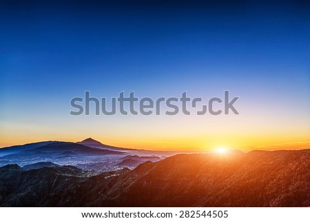 Sun with sunlight over mountains on blue sky with fog and Teide volcano on background at evening sunset in Tenerife Canary island, Spain