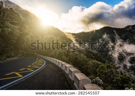 Road in mountains or rocks and sky with sun and sunlight and clouds over peak in Tenerife Canary island, Spain at sunset