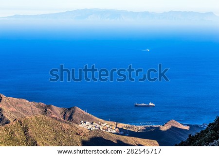 View from above from rock or mountain on ocean or sea with cargo ship. Island on background