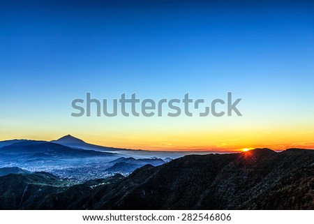 Sun over mountains on blue sky with fog or haze and Teide volcano on background at evening sunset in Tenerife Canary island, Spain
