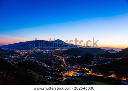 City or town with illumination after sunset or sundown at evening in mountains with blue sky and Teide volcano on background in Tenerife Canary island, Spain at spring or summer