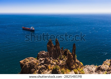 Container cargo ship and vessel on horizon in the blue ocean. View from above from rock or mountain